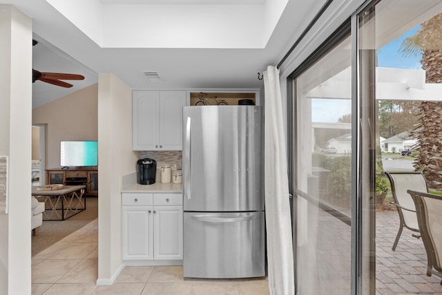 kitchen with lofted ceiling, white cabinets, tasteful backsplash, light tile patterned flooring, and stainless steel refrigerator