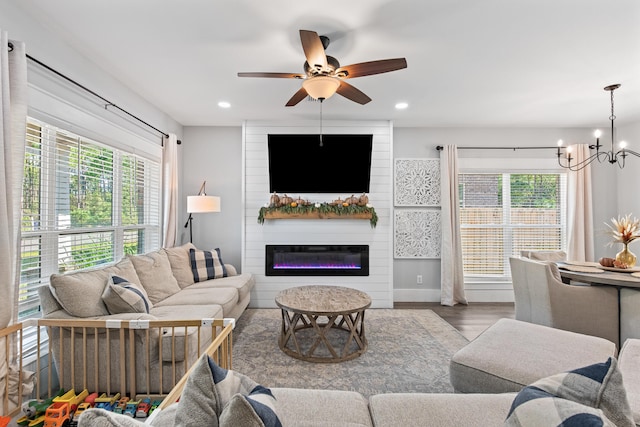 living room with ceiling fan with notable chandelier, a fireplace, wood-type flooring, and plenty of natural light