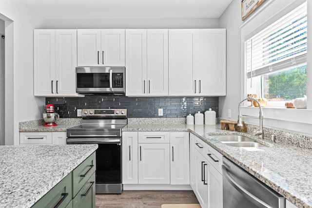 kitchen with appliances with stainless steel finishes, white cabinets, sink, and light wood-type flooring