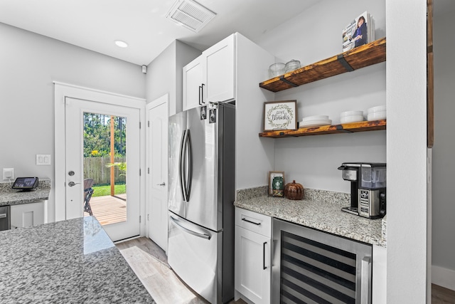 kitchen with wine cooler, stainless steel fridge, light stone countertops, light wood-type flooring, and white cabinetry