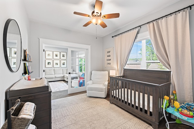 bedroom with a nursery area, light wood-type flooring, and ceiling fan