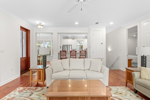 living room featuring light wood-type flooring, ceiling fan with notable chandelier, and crown molding