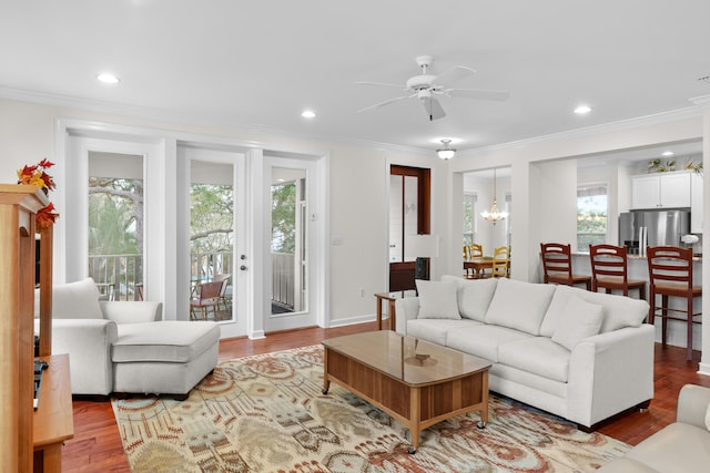 living room with a wealth of natural light, ceiling fan with notable chandelier, light hardwood / wood-style floors, and crown molding