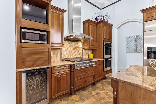 kitchen with light stone countertops, wall chimney range hood, backsplash, stainless steel appliances, and wine cooler