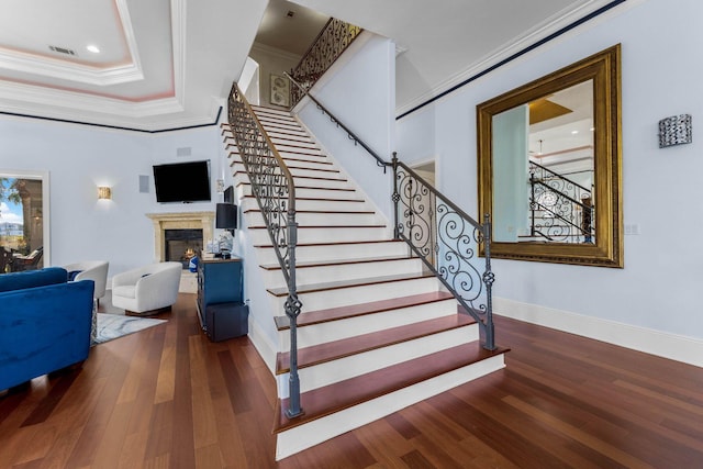 stairway featuring a tray ceiling, wood-type flooring, and ornamental molding