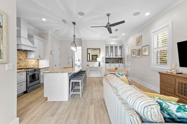 kitchen with high end range, pendant lighting, decorative backsplash, premium range hood, and a kitchen island with sink