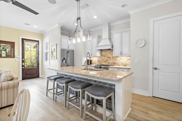 kitchen featuring appliances with stainless steel finishes, an island with sink, custom exhaust hood, white cabinets, and light hardwood / wood-style flooring