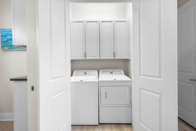 laundry area featuring washing machine and dryer, light wood-type flooring, and cabinets