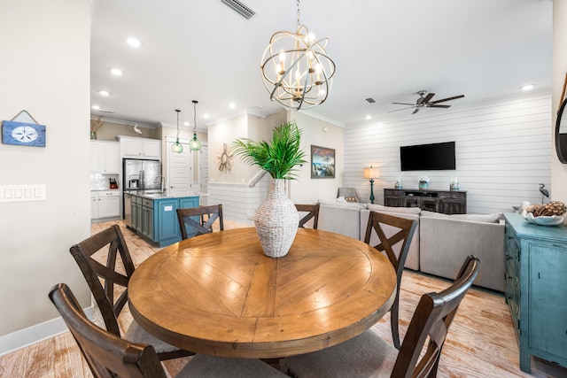 dining space with wooden walls, ornamental molding, sink, and light wood-type flooring