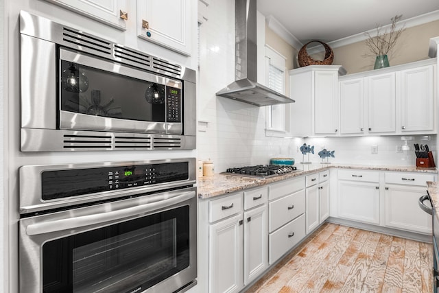 kitchen with wall chimney exhaust hood, white cabinetry, and stainless steel appliances