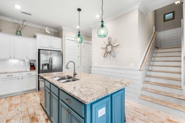 kitchen with appliances with stainless steel finishes, sink, an island with sink, white cabinets, and blue cabinetry