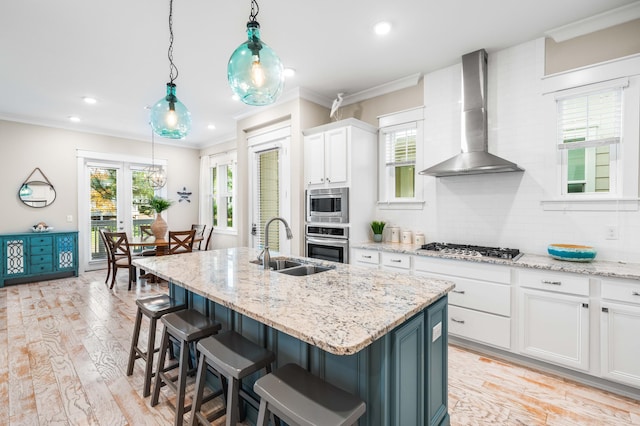 kitchen featuring wall chimney exhaust hood, white cabinetry, stainless steel appliances, and an island with sink