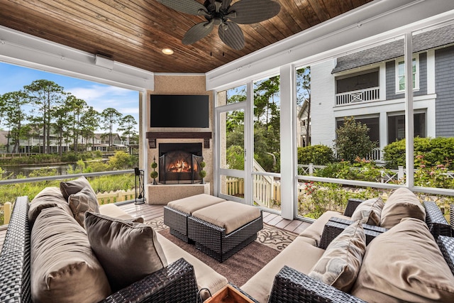 sunroom featuring an outdoor fireplace, ceiling fan, wooden ceiling, and a wealth of natural light