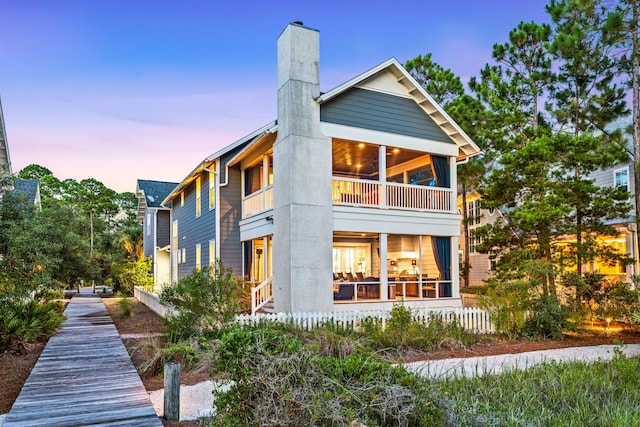 back house at dusk featuring a sunroom and a balcony