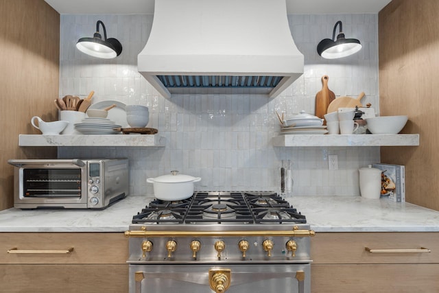 kitchen with backsplash, stainless steel stove, premium range hood, and light stone counters