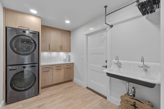 laundry room featuring cabinets, stacked washer and dryer, sink, and light hardwood / wood-style floors