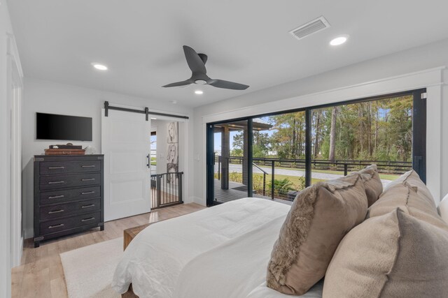 bedroom with multiple windows, light hardwood / wood-style floors, access to outside, and a barn door