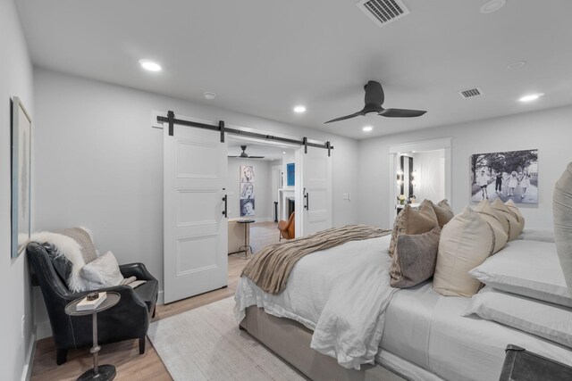 bedroom with light hardwood / wood-style floors, a barn door, and ceiling fan