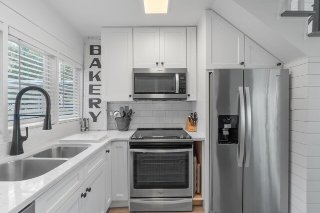kitchen featuring stainless steel appliances, sink, light stone counters, white cabinets, and decorative backsplash