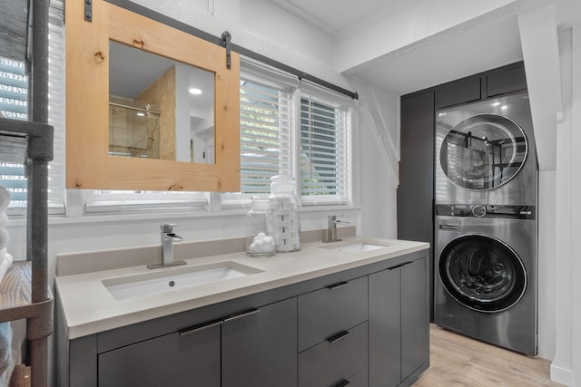 laundry room with a barn door, stacked washing maching and dryer, sink, and light wood-type flooring
