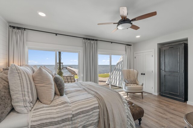 bedroom with light wood-type flooring, ceiling fan, a water view, and access to outside
