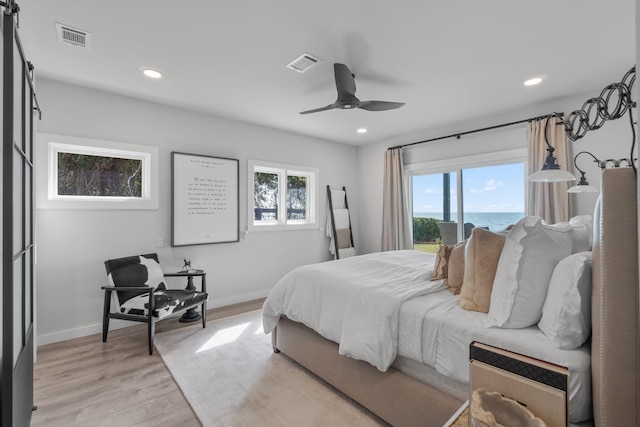 bedroom featuring light wood-type flooring, a water view, multiple windows, and ceiling fan