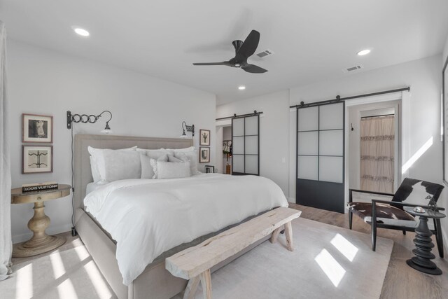 bedroom featuring light hardwood / wood-style floors, a barn door, and ceiling fan