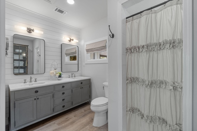 bathroom with toilet, hardwood / wood-style flooring, wooden walls, vanity, and walk in shower