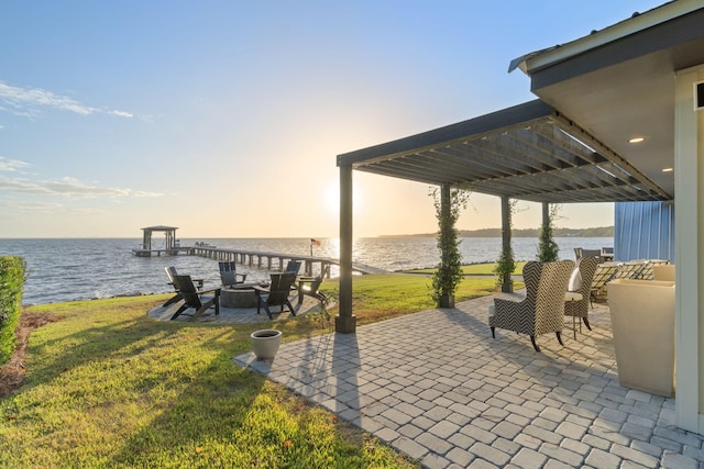patio terrace at dusk with a lawn, a water view, and a fire pit