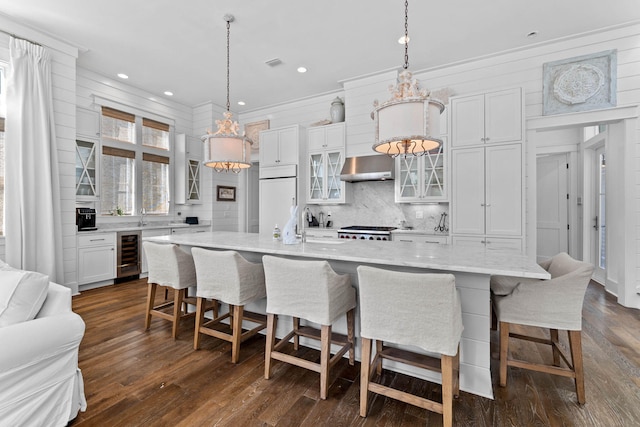 kitchen featuring wine cooler, paneled built in fridge, decorative light fixtures, and a large island with sink