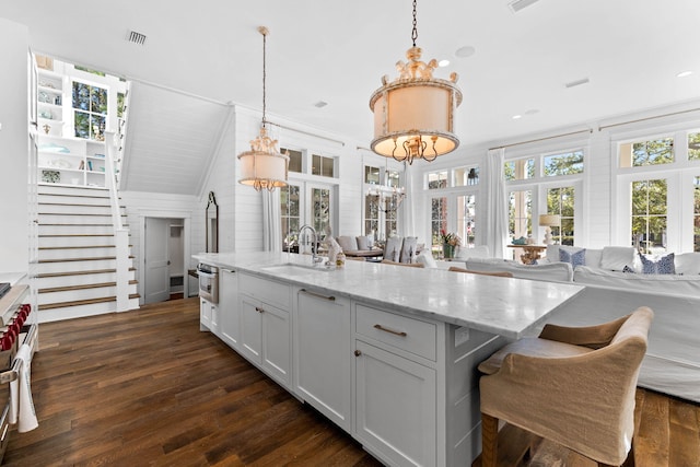 kitchen with light stone countertops, white cabinetry, sink, hanging light fixtures, and dark hardwood / wood-style floors