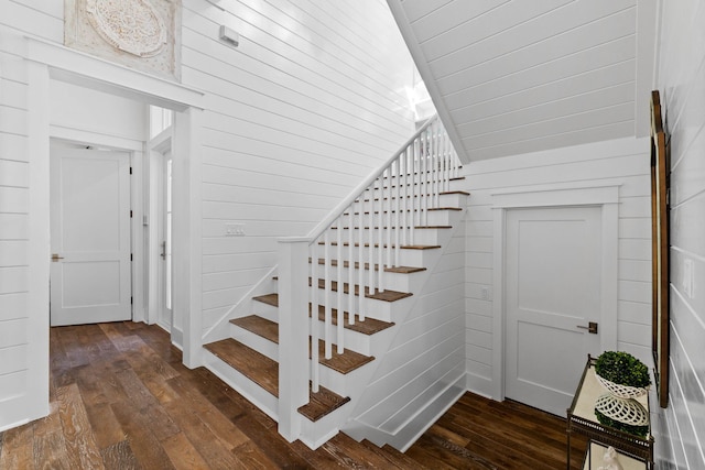 stairs with wood walls, hardwood / wood-style floors, and lofted ceiling