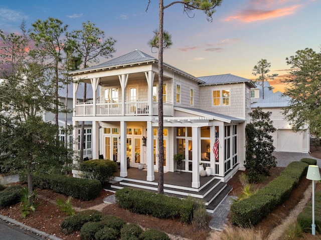 back house at dusk with french doors, a balcony, and a garage