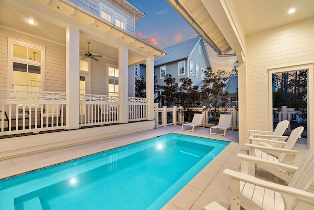 pool at dusk featuring ceiling fan and a patio