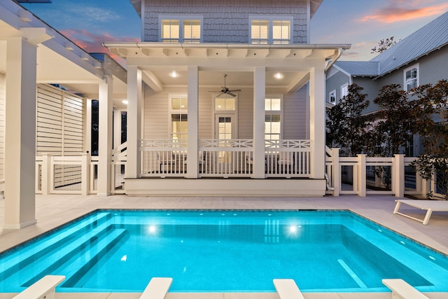 pool at dusk with ceiling fan, a diving board, and a patio area