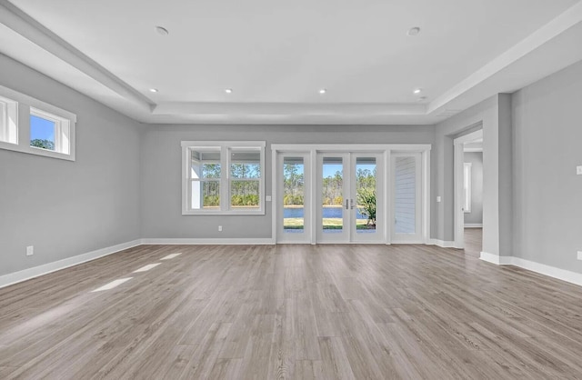 unfurnished living room featuring french doors, a tray ceiling, and light wood-type flooring