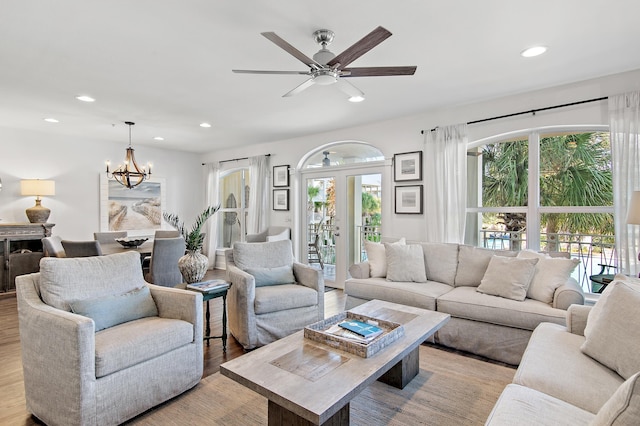 living room featuring light hardwood / wood-style flooring, ceiling fan with notable chandelier, and plenty of natural light