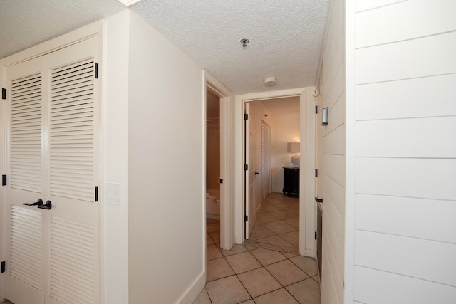 hallway with a textured ceiling and light tile patterned floors