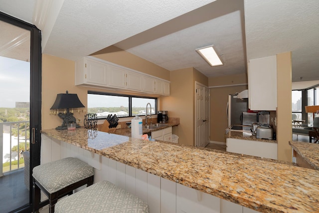 kitchen featuring light stone countertops, sink, a textured ceiling, kitchen peninsula, and white cabinets