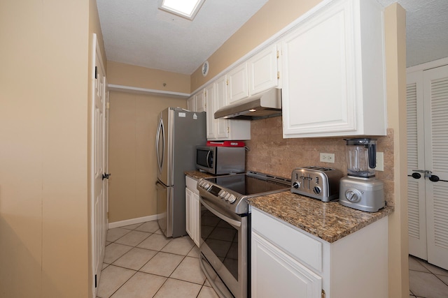 kitchen with tasteful backsplash, light tile patterned flooring, stainless steel appliances, white cabinets, and dark stone countertops