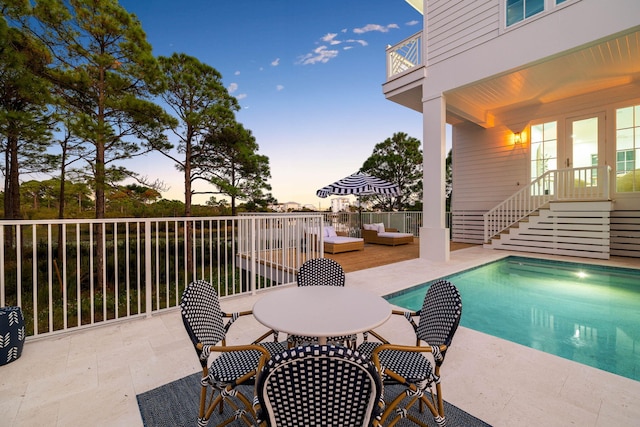 pool at dusk featuring french doors and a patio area