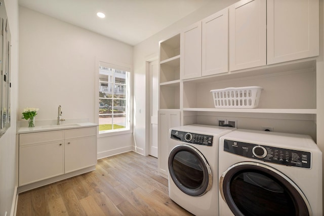 washroom with light hardwood / wood-style floors, washer and dryer, sink, and cabinets