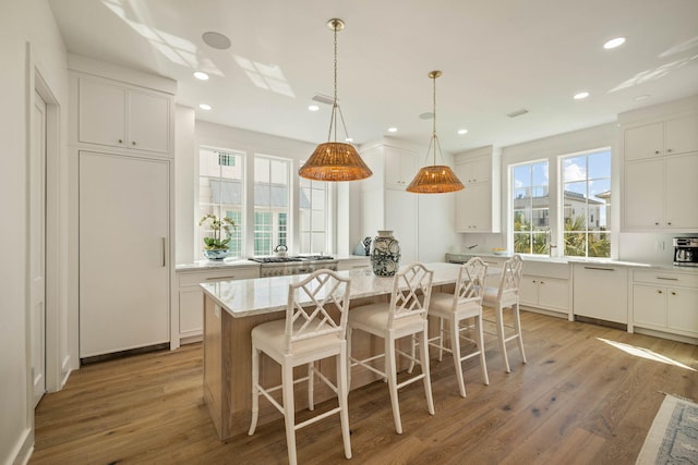 kitchen with light stone countertops, a center island, hanging light fixtures, light hardwood / wood-style floors, and white cabinets