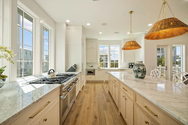 kitchen featuring light stone countertops, light brown cabinetry, high end stainless steel range, light hardwood / wood-style floors, and decorative light fixtures