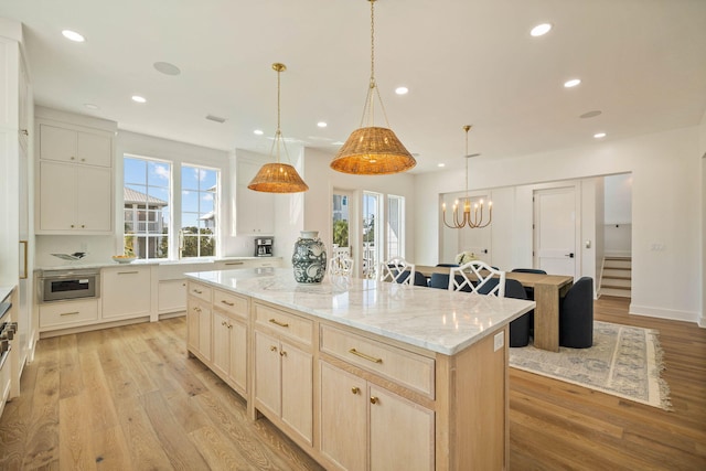 kitchen featuring light stone countertops, a spacious island, decorative light fixtures, light hardwood / wood-style flooring, and an inviting chandelier