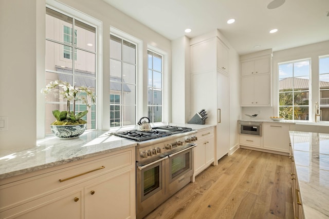 kitchen featuring appliances with stainless steel finishes, light hardwood / wood-style flooring, white cabinets, and light stone counters