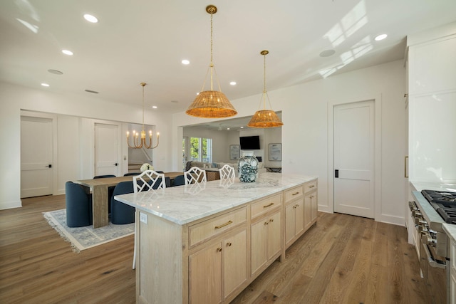 kitchen featuring light brown cabinets, a kitchen island, a kitchen bar, light hardwood / wood-style flooring, and light stone counters