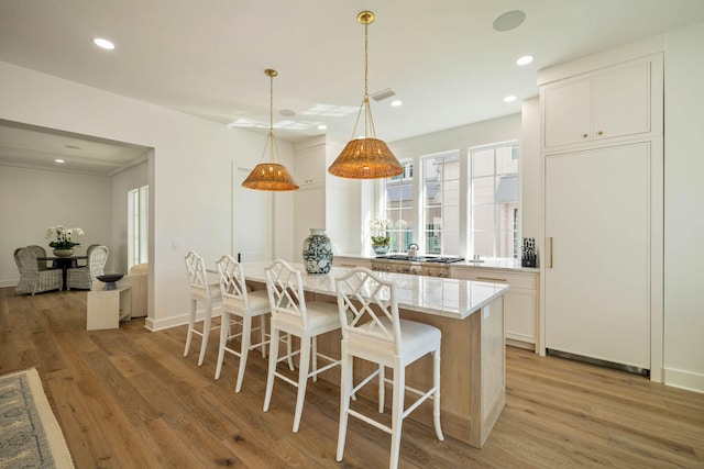 kitchen featuring a center island, pendant lighting, light wood-type flooring, white cabinetry, and light stone counters