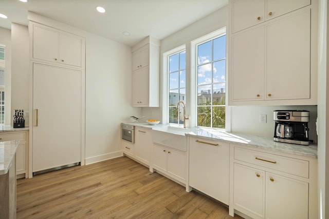 kitchen with light stone countertops, light wood-type flooring, and white cabinets