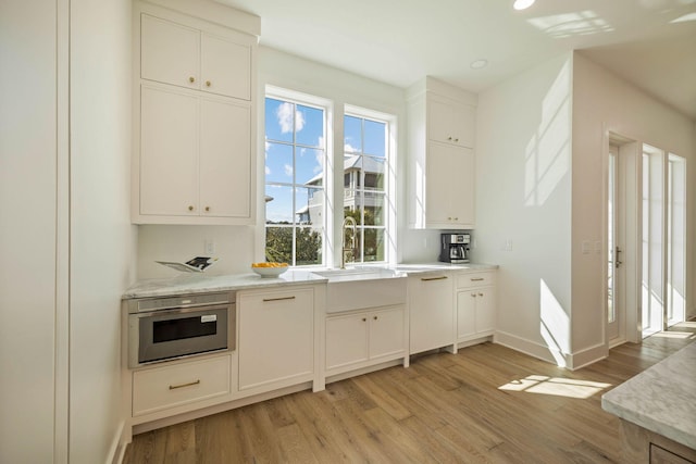 bar with oven, white cabinetry, light stone countertops, light hardwood / wood-style flooring, and sink